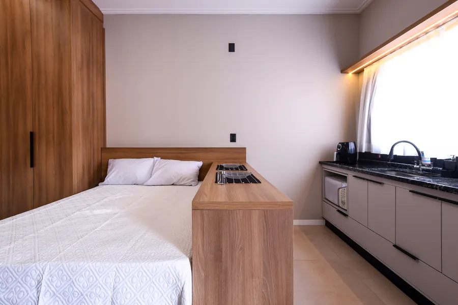 Cama e cozinha com bancada em madeira.
