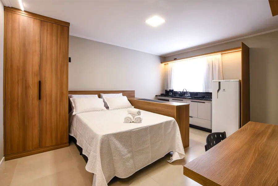 Cama com enxoval branco junto à cozinha e bancada.
